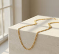 Gold chain necklace on a light stone surface with a soft background