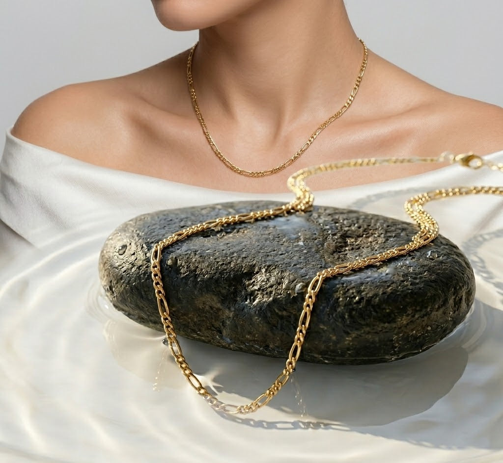 Gold necklace draped over a stone with a soft, neutral background